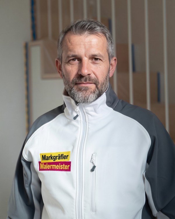 Henryk Knichalla, Leiter Bauausführung, im Markgräfler Malermeisterbetrieb Arbeitsjacke vor einer unfertigen Holztreppe